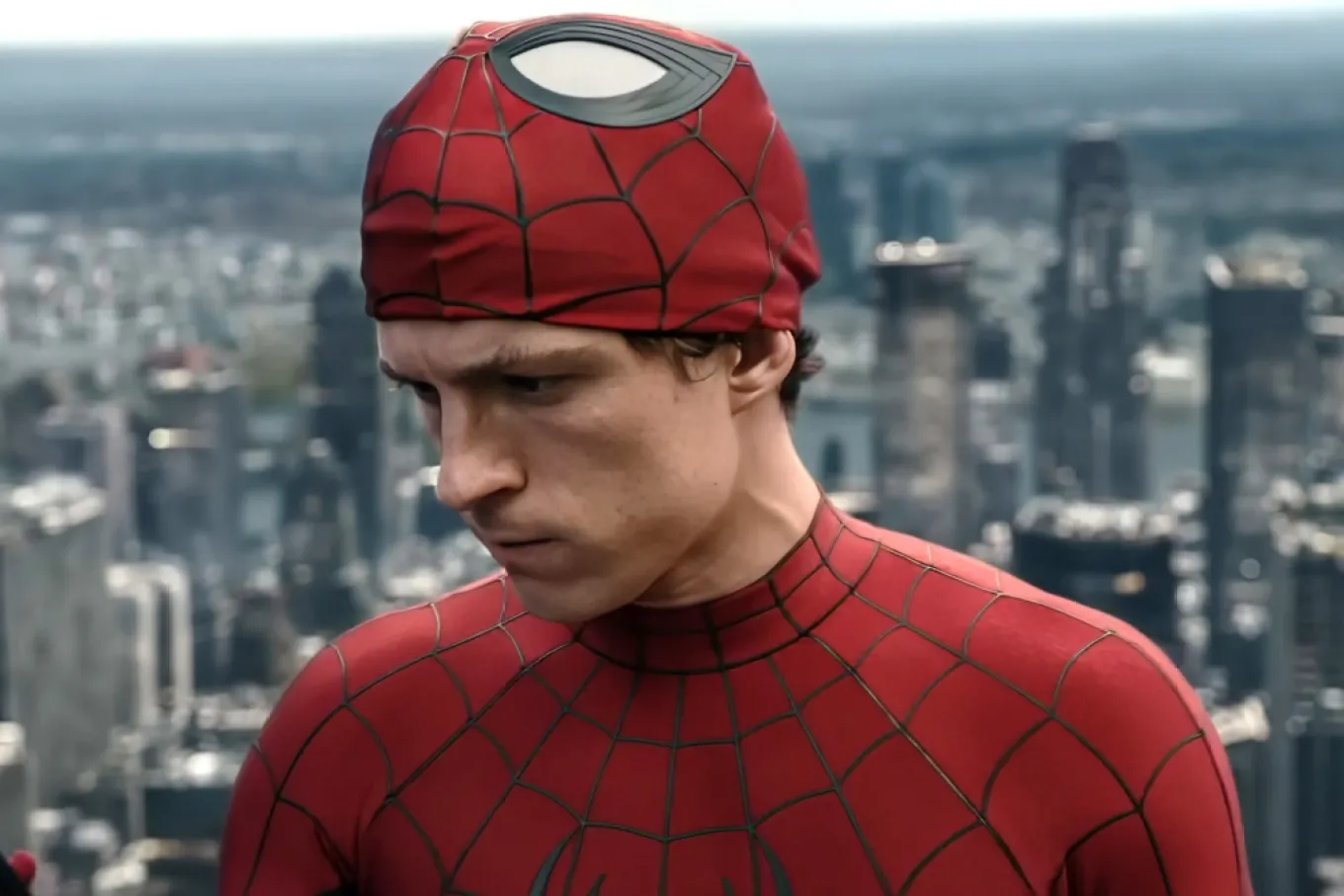 Close-up of Spider-man in a Red Suit with Web Patterns, Looking Down with a Blurred City Skyline in the Background.