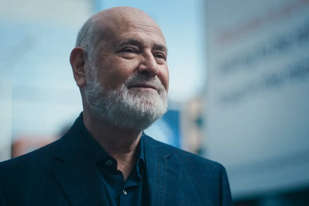 Rob Riener Smiling with a White Beard in a Dark Suit, Against a Blurred Blue Backdrop in Fx's 'the Bear'