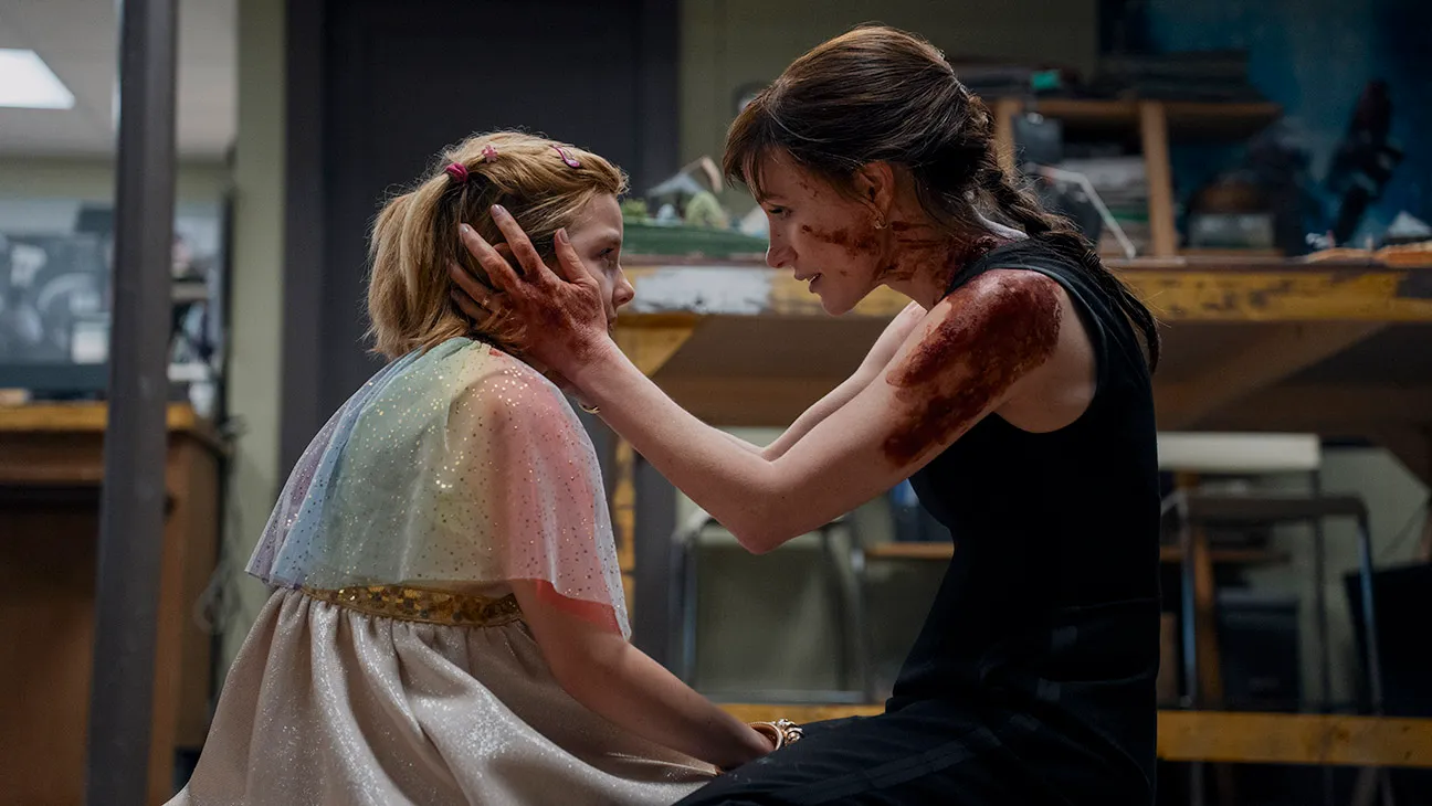 Woman in a Black Dress Gently Consoles a Girl in a Sparkly Pastel Dress, Cupping Her Face in a Workshop Setting.