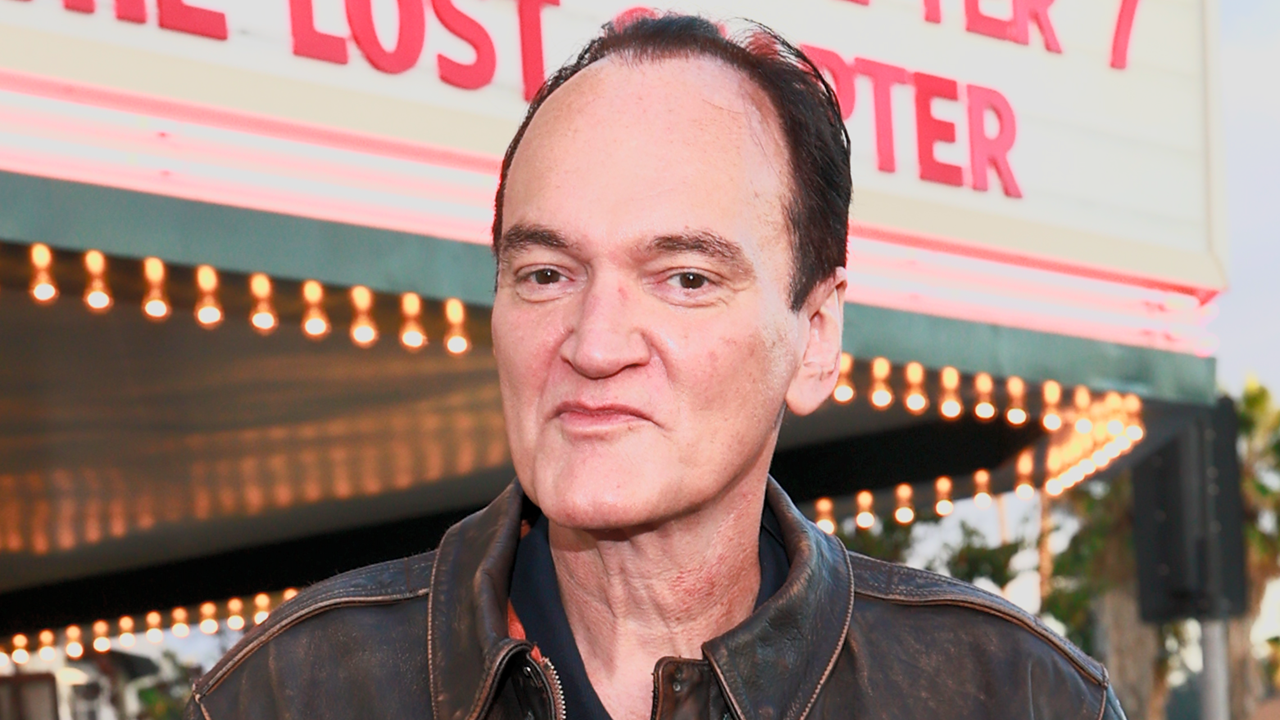 Quentin-tarantino-says-hes-written-a-script-for-10th-and-fin_tumjjpg | the Cinema Group Man in a Brown Leather Jacket Stands Outdoors at a Venue with Marquee Lights Behind Him, Smiling Subtly